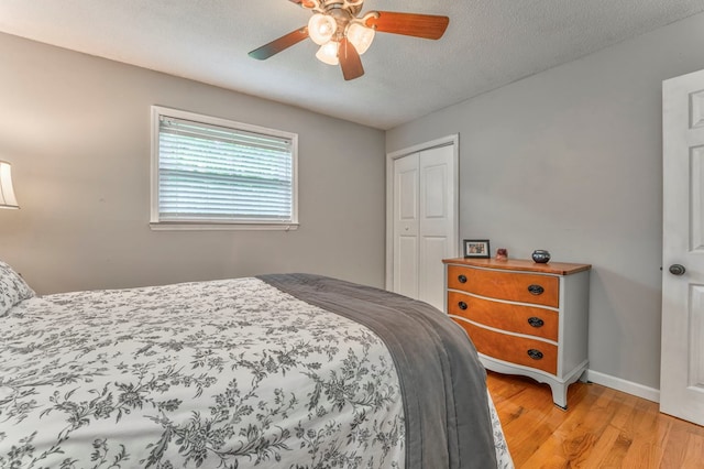 bedroom featuring a closet, light wood-style floors, baseboards, ceiling fan, and a textured ceiling