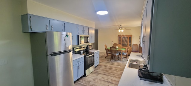 kitchen featuring blue cabinetry, sink, appliances with stainless steel finishes, ceiling fan, and light hardwood / wood-style floors