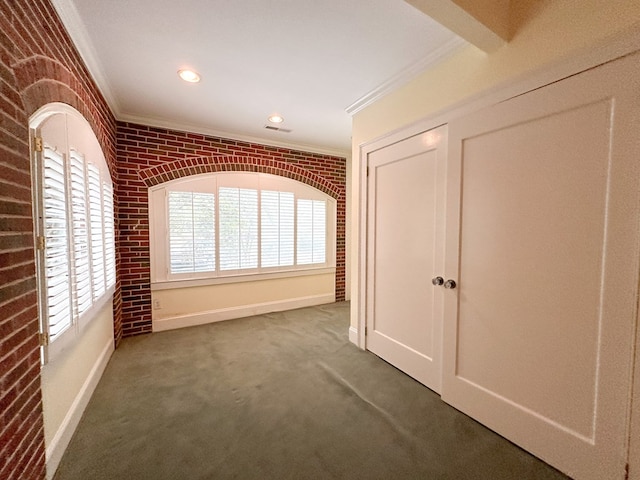 interior space featuring dark colored carpet, ornamental molding, and brick wall