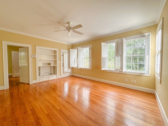 spare room with crown molding, a healthy amount of sunlight, built in features, and light wood-type flooring