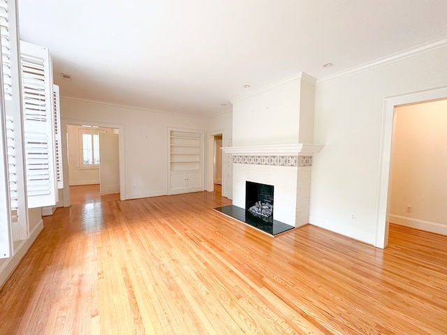 unfurnished living room with a tiled fireplace, ornamental molding, built in features, and light hardwood / wood-style floors