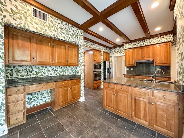 kitchen featuring sink, built in desk, dark stone counters, stainless steel appliances, and beam ceiling