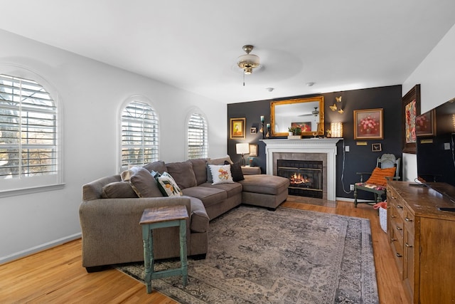 living area featuring a ceiling fan, a tile fireplace, baseboards, and light wood finished floors