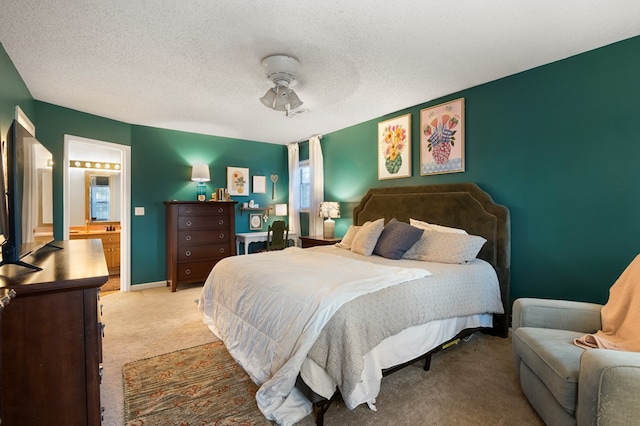 carpeted bedroom featuring a textured ceiling, ensuite bathroom, a ceiling fan, and baseboards