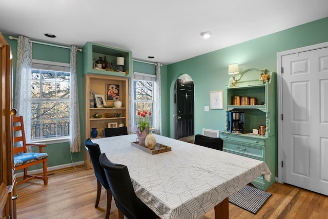 dining area featuring light wood-type flooring, visible vents, arched walkways, and baseboards