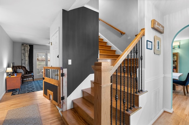 staircase with baseboards, visible vents, arched walkways, and wood finished floors