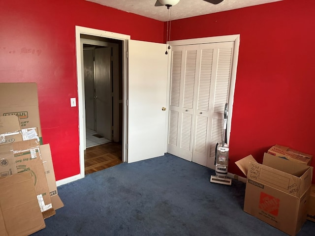 unfurnished bedroom featuring ceiling fan, dark carpet, a closet, and a textured ceiling