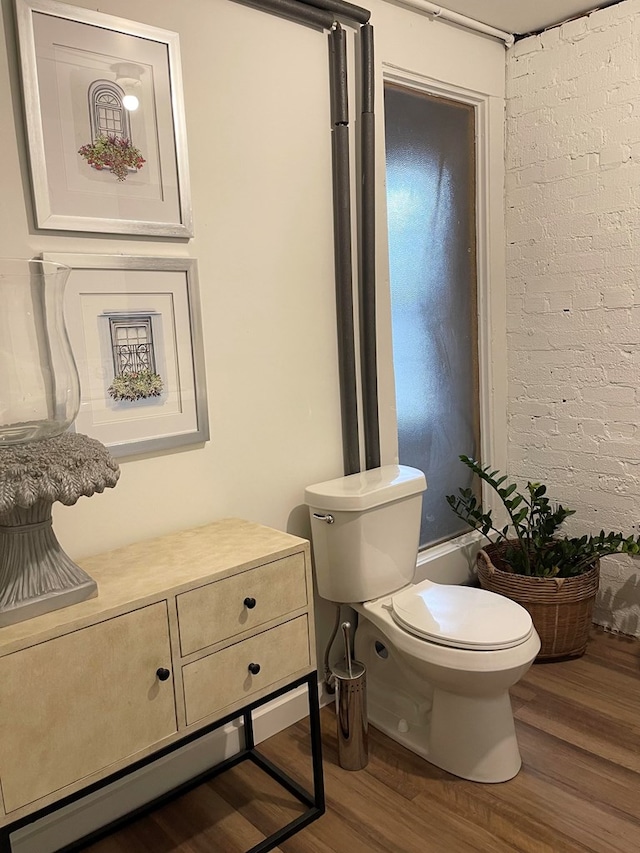 bathroom featuring brick wall, hardwood / wood-style floors, and toilet