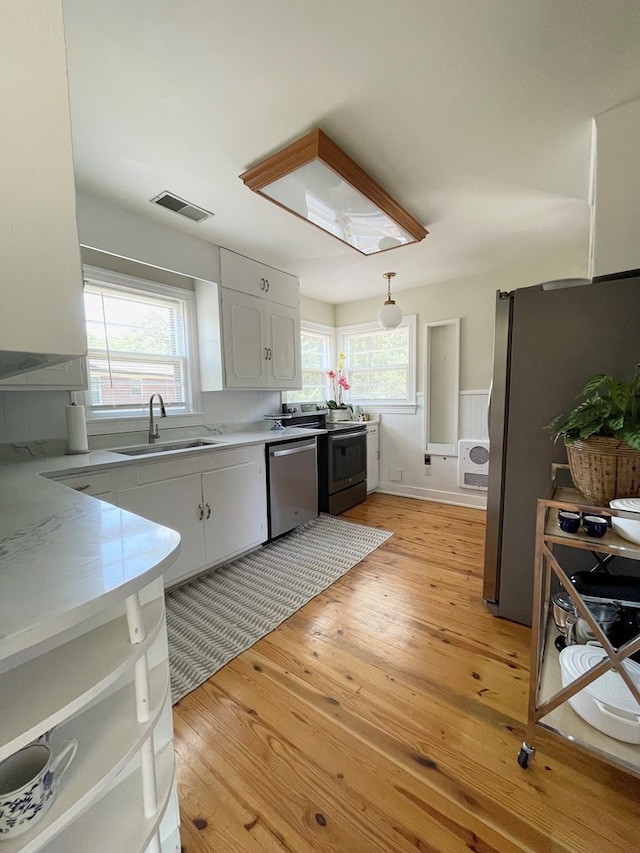 kitchen with sink, white cabinetry, decorative light fixtures, light wood-type flooring, and stainless steel appliances