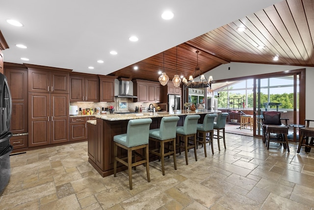 kitchen featuring decorative light fixtures, an island with sink, wood ceiling, light stone counters, and wall chimney exhaust hood