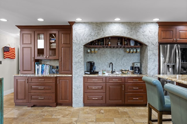 bar featuring stainless steel refrigerator with ice dispenser, sink, crown molding, light stone counters, and decorative backsplash