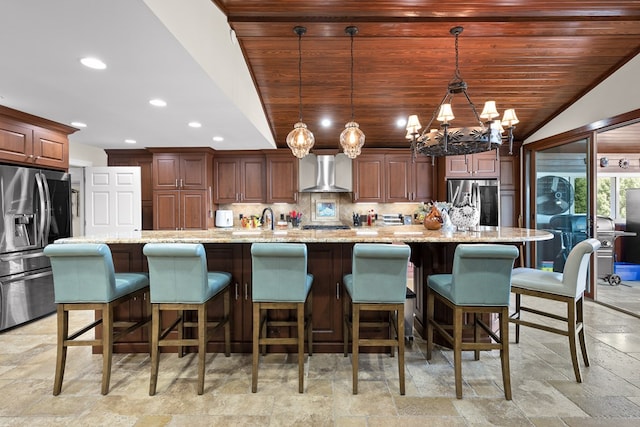 kitchen with decorative light fixtures, a large island with sink, stainless steel fridge with ice dispenser, and wall chimney range hood