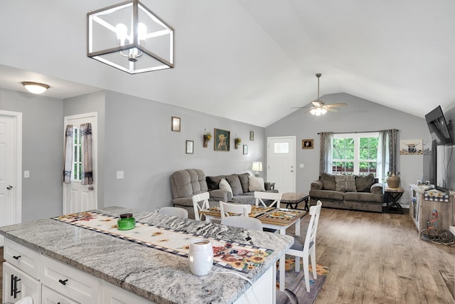 interior space with white cabinetry, decorative light fixtures, vaulted ceiling, light stone countertops, and hardwood / wood-style floors