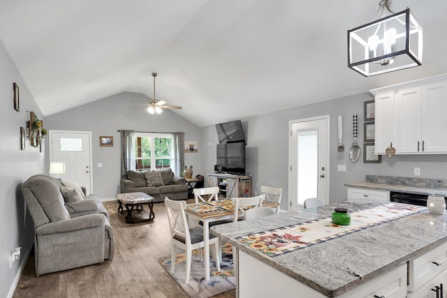 kitchen with lofted ceiling, ceiling fan, white cabinetry, light stone counters, and light wood-type flooring