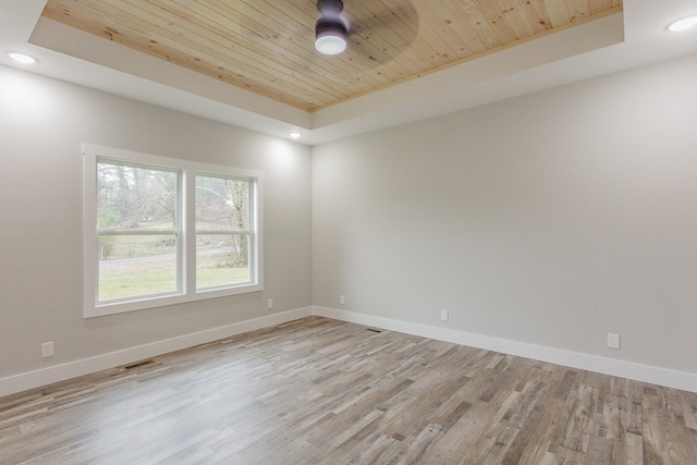 spare room with a raised ceiling, light wood-type flooring, and wooden ceiling