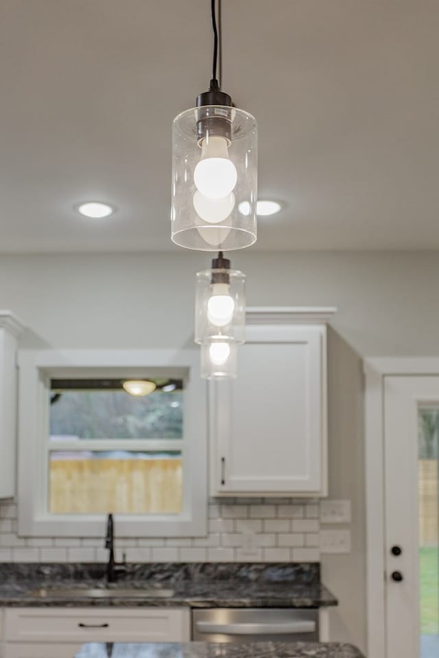 interior details featuring tasteful backsplash, dark stone counters, hanging light fixtures, and white cabinets