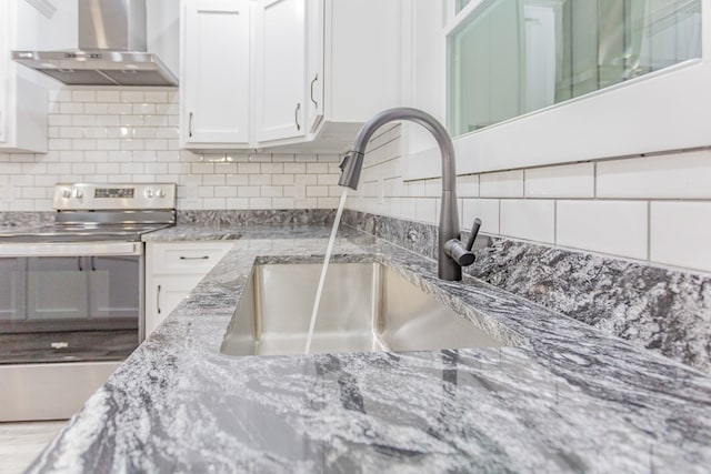 room details featuring wall chimney range hood, sink, white cabinetry, tasteful backsplash, and stainless steel electric range oven