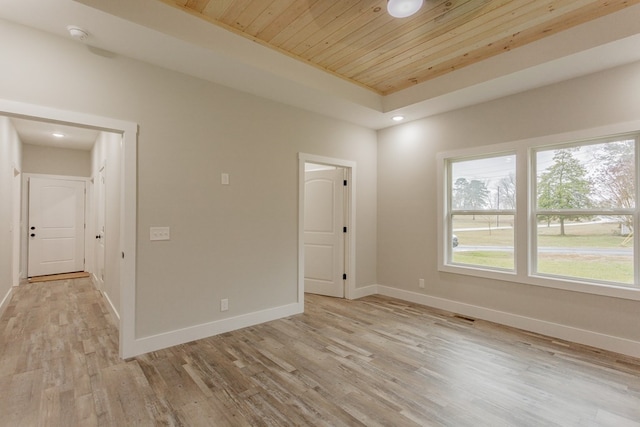 spare room with a raised ceiling, light hardwood / wood-style floors, and wooden ceiling