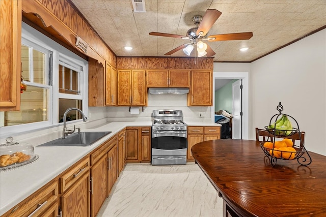 kitchen with under cabinet range hood, a sink, gas stove, crown molding, and brown cabinetry