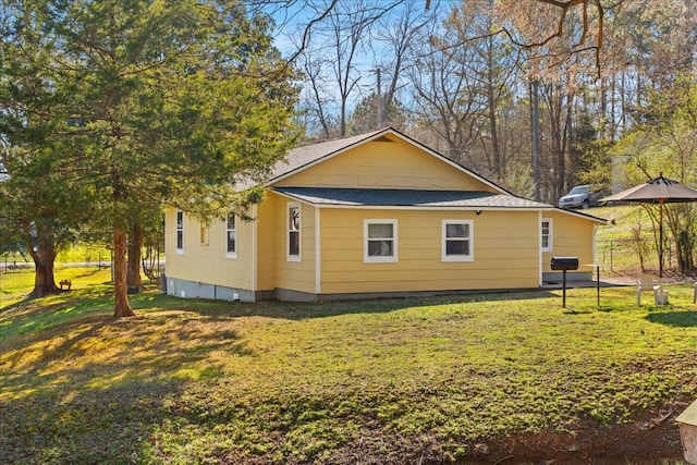 view of side of property featuring a lawn, a shingled roof, and fence