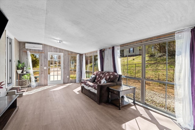 living area with vaulted ceiling, wood finished floors, a wall mounted air conditioner, and a textured ceiling