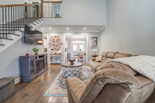 living room with crown molding, a towering ceiling, a chandelier, and dark hardwood / wood-style flooring