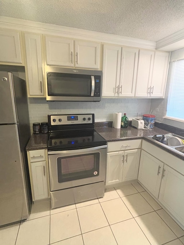 kitchen with a textured ceiling, light tile patterned flooring, a sink, appliances with stainless steel finishes, and backsplash