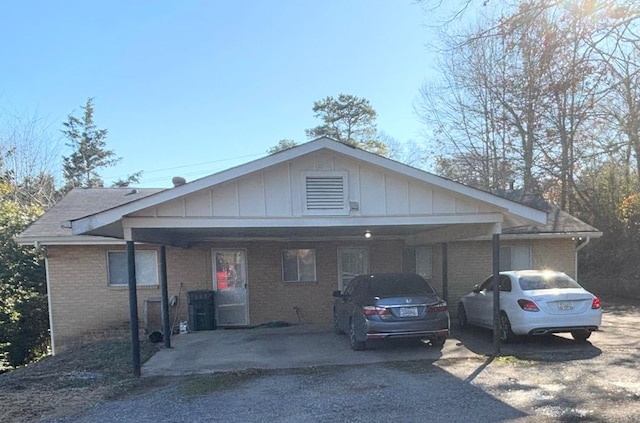 view of front facade featuring board and batten siding, brick siding, driveway, and a carport