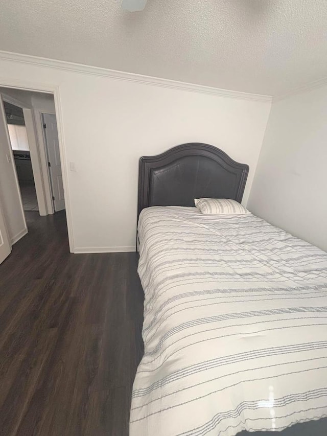 bedroom featuring dark wood-style floors, ornamental molding, a textured ceiling, and baseboards