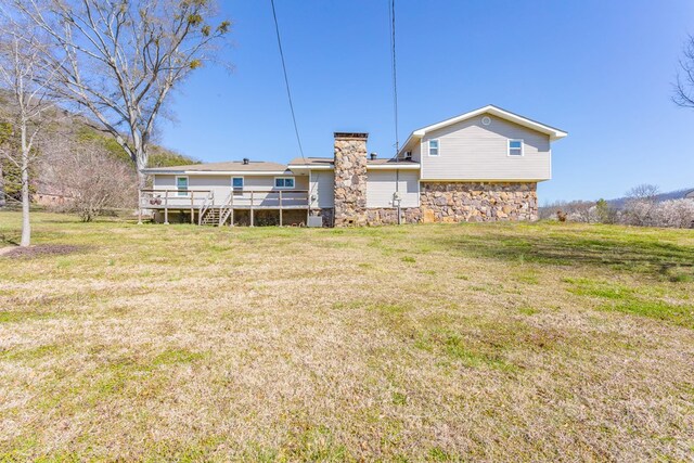 rear view of house with a chimney, stone siding, a wooden deck, and a yard