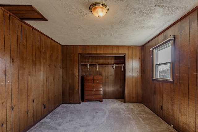 unfurnished bedroom featuring a textured ceiling, wooden walls, a closet, and light carpet