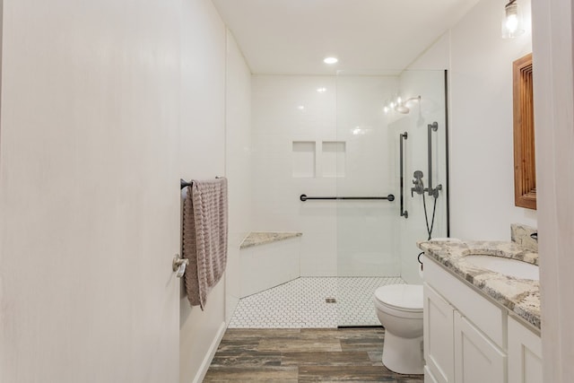 bathroom featuring vanity, toilet, wood finished floors, and tiled shower