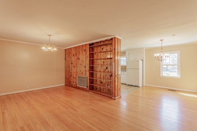 spare room with an inviting chandelier, ornamental molding, and light wood finished floors