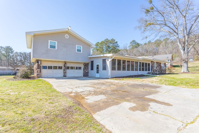 view of front facade with an attached garage, driveway, a front yard, and a sunroom