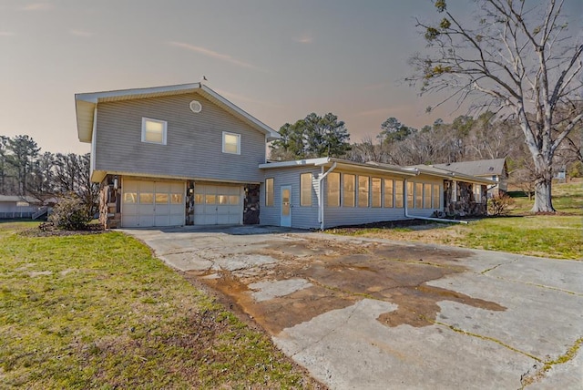 view of front facade featuring a front yard, a sunroom, an attached garage, and driveway