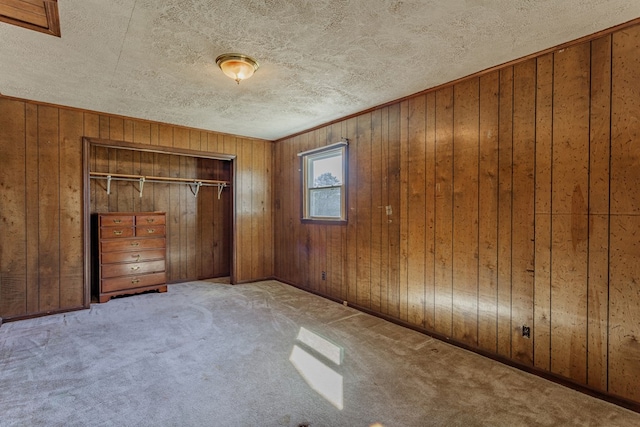 unfurnished bedroom with a closet, carpet floors, a textured ceiling, and wooden walls