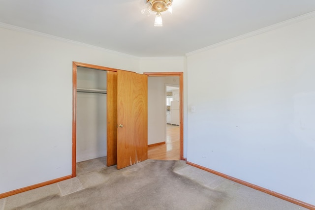 unfurnished bedroom with ornamental molding, freestanding refrigerator, a closet, carpet flooring, and baseboards