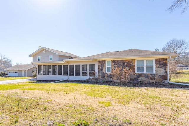 back of property with stone siding, a lawn, and a sunroom