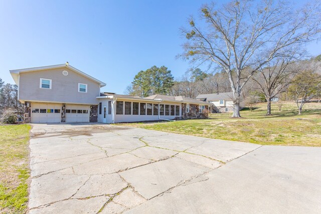 view of front of house featuring a garage, concrete driveway, a front yard, and a sunroom