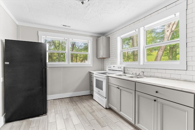 kitchen with gray cabinets, freestanding refrigerator, electric stove, light wood-style floors, and tasteful backsplash