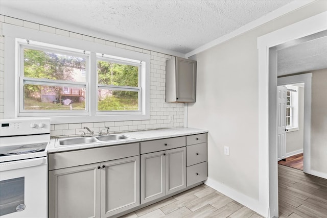 kitchen with gray cabinetry, a sink, backsplash, white electric range oven, and light wood-style floors