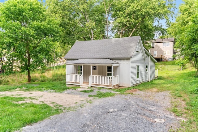 view of front of home with board and batten siding, a front yard, covered porch, and roof with shingles