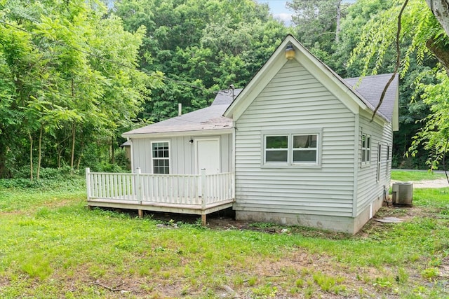 back of house with a wooded view, central AC, roof with shingles, a lawn, and a deck