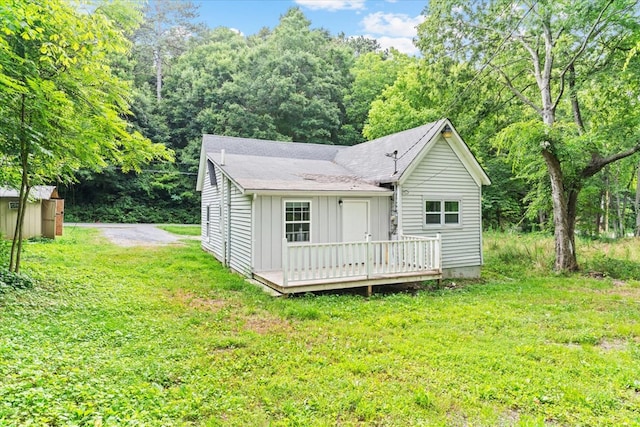 view of front facade featuring a shingled roof, a front yard, board and batten siding, and a wooden deck