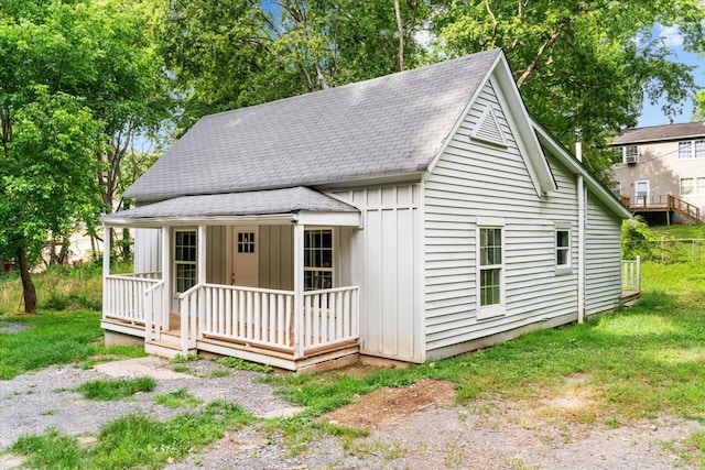 view of front facade with covered porch, board and batten siding, a front yard, and roof with shingles