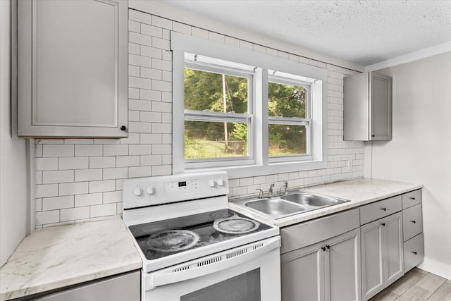 kitchen featuring white range with electric cooktop, decorative backsplash, gray cabinets, and a sink