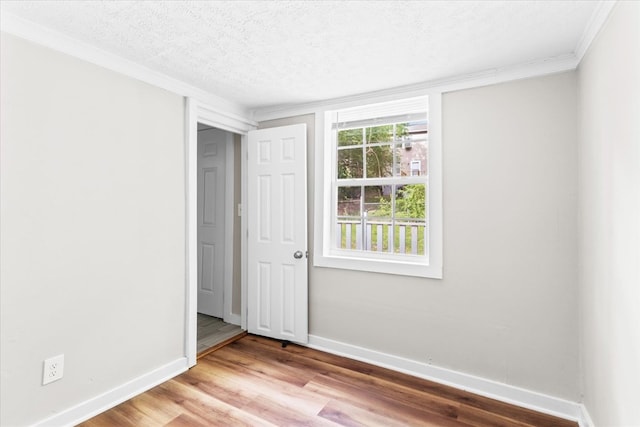 spare room with ornamental molding, a textured ceiling, baseboards, and wood finished floors