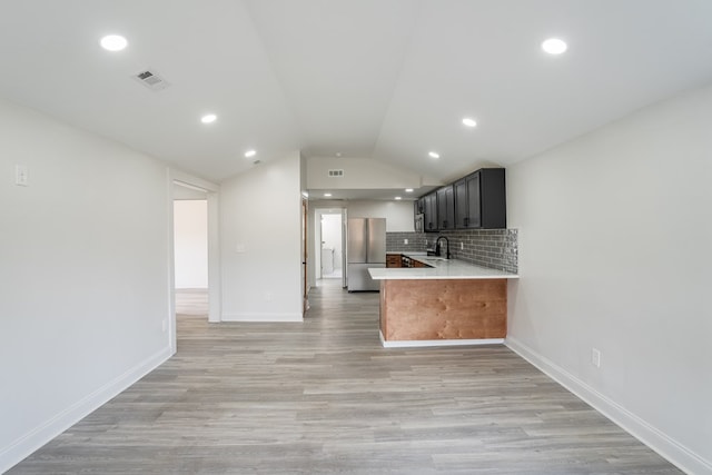 kitchen featuring light countertops, backsplash, appliances with stainless steel finishes, vaulted ceiling, and a peninsula