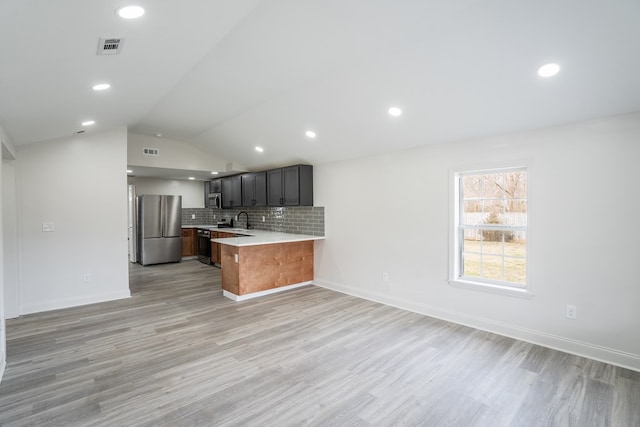 kitchen featuring tasteful backsplash, lofted ceiling, appliances with stainless steel finishes, a peninsula, and light countertops