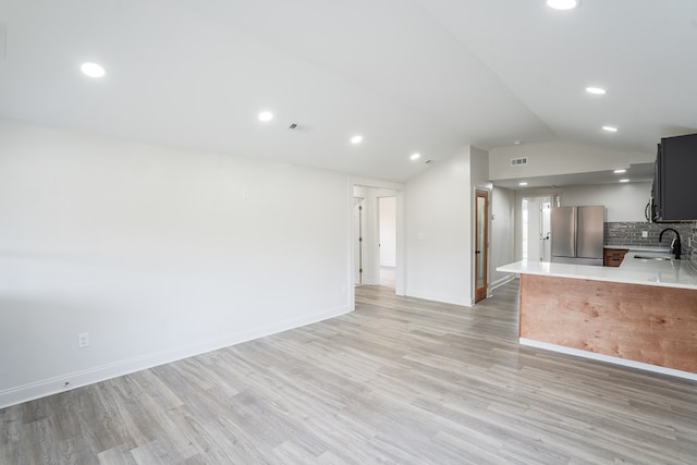 kitchen with freestanding refrigerator, a peninsula, vaulted ceiling, light countertops, and light wood-style floors